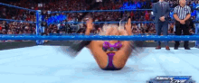a woman is laying on her back in a wrestling ring while a referee looks on .