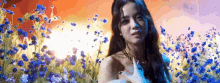 a woman is standing in a field of blue flowers and looking at the camera .