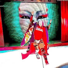 a wrestler wearing a red shirt and a purple cape is walking on a stage .