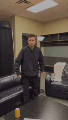 a man in a black jacket is standing in a living room with a can of soda on the table
