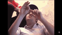 a man is laying down with his hands on his face and making a peace sign .