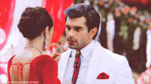 a man in a white suit and red tie looks at a woman in a red blouse