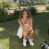 a woman in a white dress and white shoes is sitting on a bench in the grass .