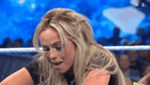a woman with long blonde hair is sitting in a wrestling ring with her mouth open .