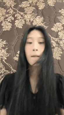 a woman with long black hair is standing in front of a floral blanket .