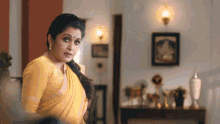 a woman in a yellow saree is standing in a living room