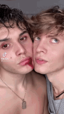 two young men are standing next to each other and one has blood on his face and the other has a necklace around his neck