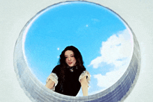 a woman in a black top is looking through a hole in a wall at the sky