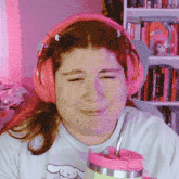 a woman wearing pink headphones holds a cup with a straw in it
