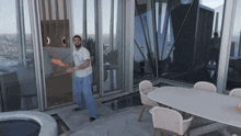 a man in a white t-shirt is standing in front of a large window holding a frisbee