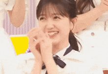 a girl in a white shirt and blue tie is smiling with her hands folded .