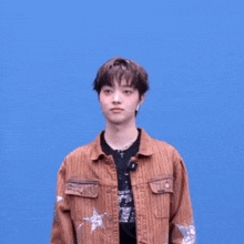 a young man wearing a brown jacket with stars on the sleeves is making a funny face