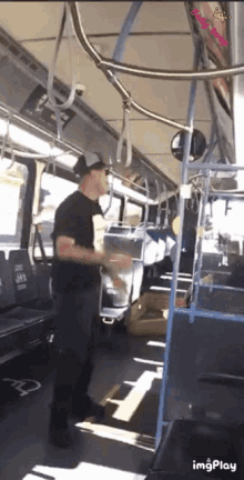 a man in a black shirt is standing on a bus with the word imgplay on the bottom