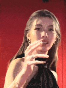 a woman in a black dress is standing in front of a red curtain and holding something in her hand .