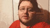 a man with glasses and a red shirt is making a funny face