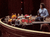 a man singing into a microphone while playing drums in front of a stage