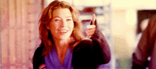 a woman is giving a thumbs up and smiling while holding a glass of wine .