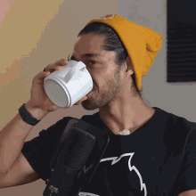 a man wearing a yellow beanie is drinking from a mug