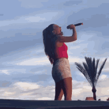 a woman is singing into a microphone with palm trees in the background