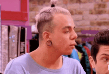 a man with a bun on his head is wearing a blue shirt and ear piercings .