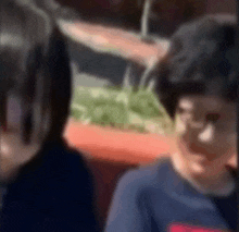 a blurry picture of two children sitting next to each other . one of the children is wearing glasses .