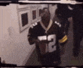 a man in a green bay packers jersey is standing in a hallway holding a football .