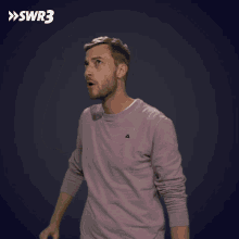 a man wearing a purple sweater is pointing up with the swr3 logo behind him
