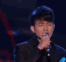 a young man is singing into a microphone on a stage .