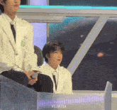 a man in a white suit and tie is sitting next to another man in a black suit and tie .