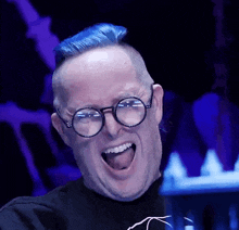 a man with blue hair and glasses is smiling with his tongue out