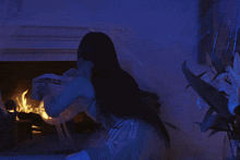 a woman is sitting in front of a fireplace in a blue room