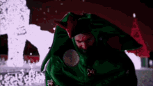 a man in a green elf costume is standing in front of a christmas tree