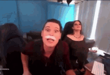 a man with a fake mustache is sitting next to a woman on a video call .