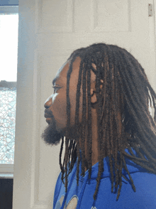 a man with dreadlocks and a beard wears a blue kappa hoodie