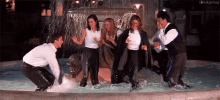 a group of people are standing in a fountain with their clothes on .
