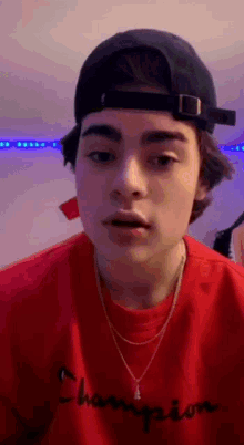 a young man wearing a hat and a red shirt is making a face .