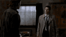 a man in a trench coat and tie is standing in front of a window with the words `` hug fail '' written above him .