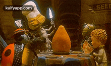a group of cartoon characters are sitting at a table with a chef holding a knife .