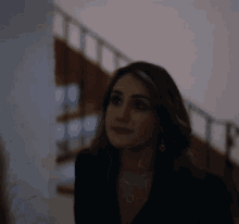 a woman wearing a black jacket and earrings is standing in front of a staircase