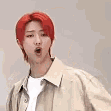 a young man with red hair is making a funny face while wearing a tan jacket and a white shirt .