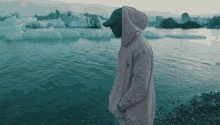 a man in a pink hoodie is standing on a beach near a body of water