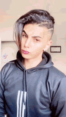 a young man with a very short haircut is wearing a black adidas hoodie .