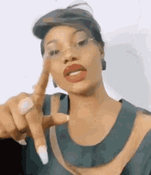a woman wearing glasses and red lipstick is pointing at the camera with her finger .