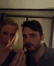 a man and a woman are standing next to each other and the woman is applying makeup to the man 's face .