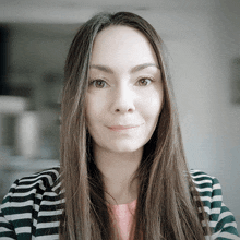 a woman with long hair wearing a striped jacket smiles for the camera