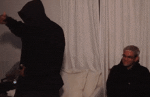 a man in a black hoodie is standing next to another man in glasses