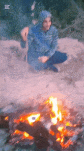 a man in a blue jacket is kneeling next to a fire