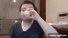 a man is drinking from a glass while sitting in front of a samsung printer .