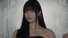 a woman with long black hair and bangs is wearing a black strapless dress and earrings .