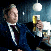 a man in a suit and tie is holding a glass of beer in his hand